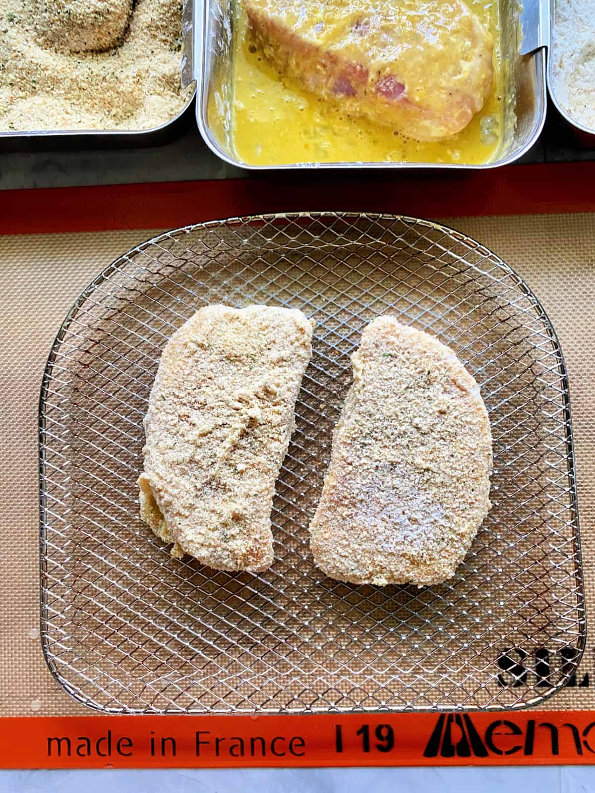 Top view of breaded pork chops on a wire rack sitting on a silicone SILPAT mat.