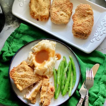 Top view of a white plate filled with pork chop slices, mashed potatoes, and green beans with pork chops on a platter next to it.