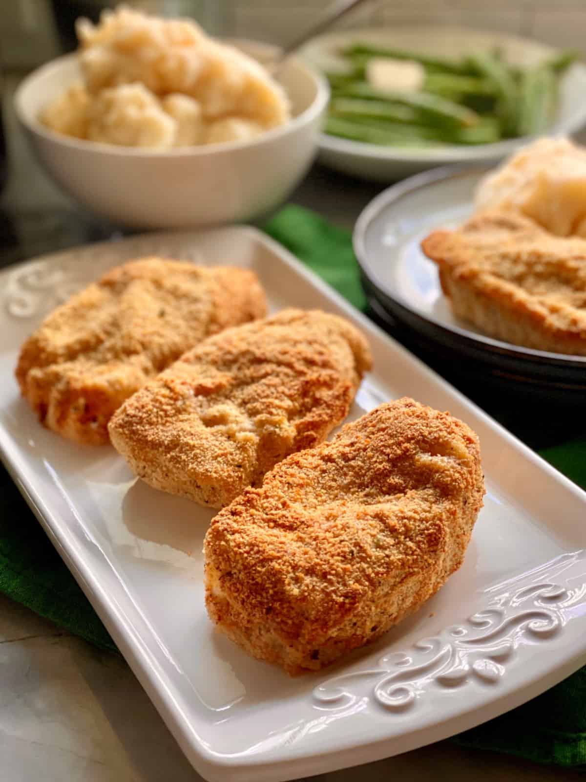 White platter with three breaded pork chops with mashed potatoes in the background.