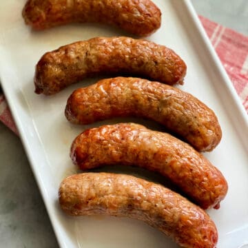 Top view of 5 crispy sausage links on a white platter with red and white striped napkin underneath it