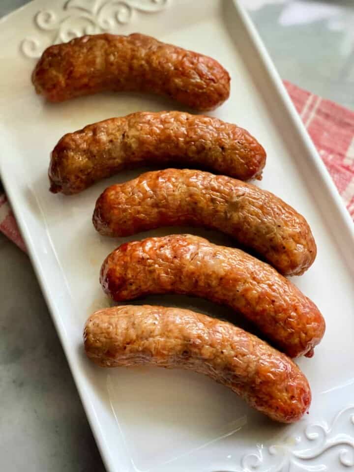 Top view of 5 crispy sausage links on a white platter with red and white striped napkin underneath it