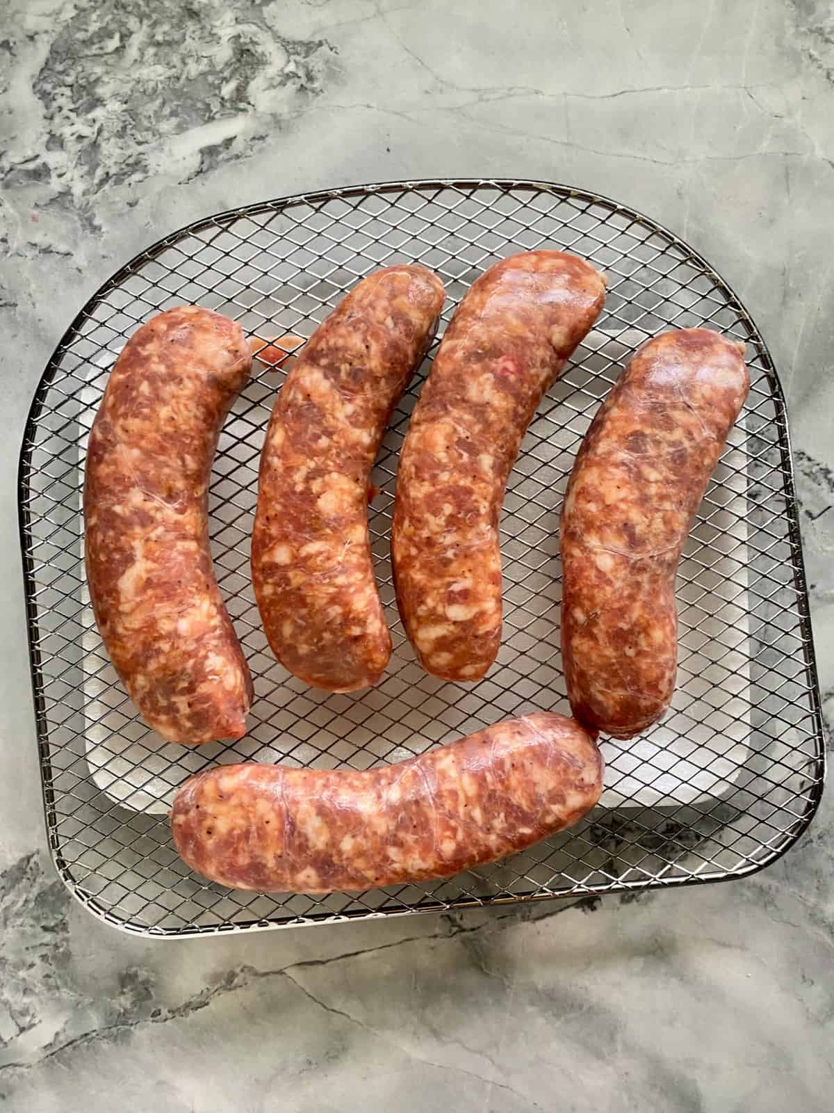 Top view of five raw sausage links on a wire rack.