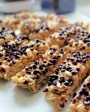 Homemade granola bars with mini chocolate chips lined up on parchment papered countertop.