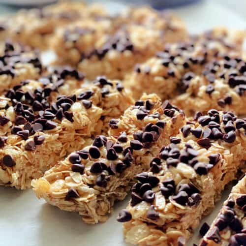 Homemade granola bars with mini chocolate chips lined up on parchment papered countertop.