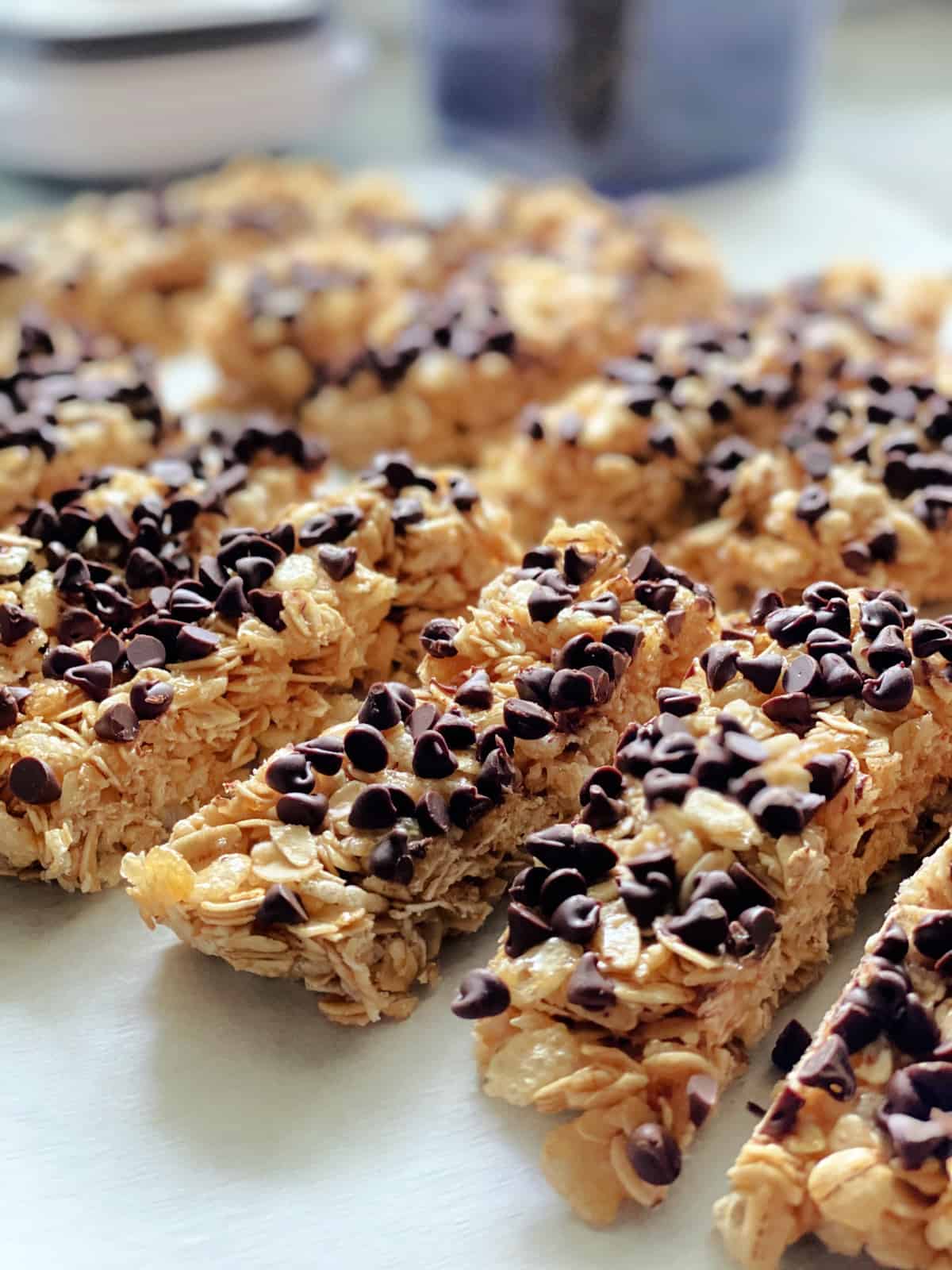 Homemade granola bars with mini chocolate chips lined up on parchment papered countertop.