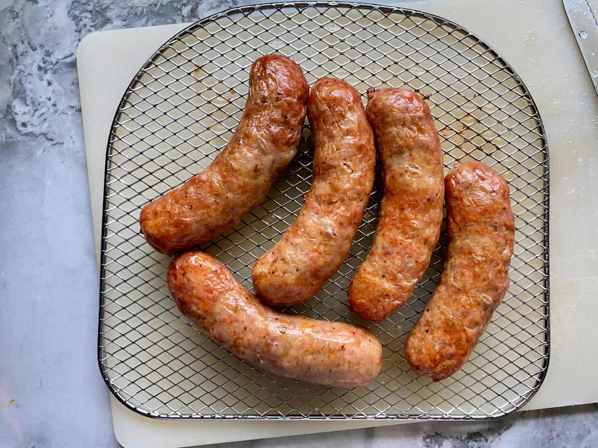 Top view of a wire rack with five crispy sausage links resting on top of a white cutting board.