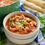 Two white bowls stacked filled with minestrone soup topped with shredded cheese and parsley.
