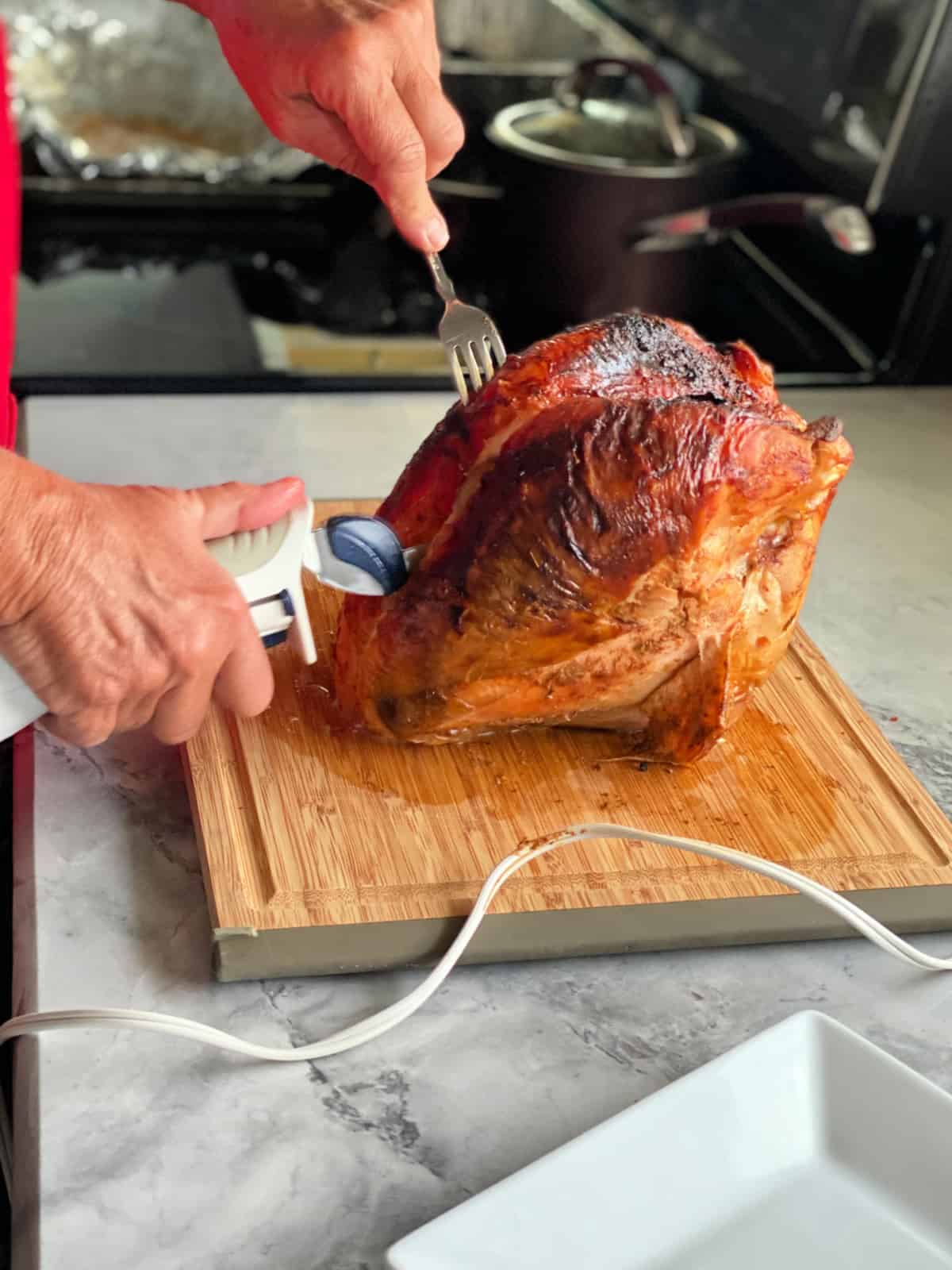 Female hand carving a full browned turkey breast on a wooden cutting board.