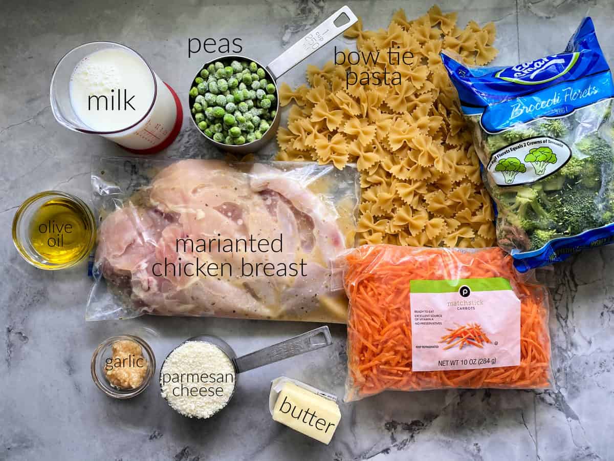 Ingredients on counter: pasta, chicken breast, carrots, broccoli, butter, parmesan, garlic, olive oil, milk, and peas.