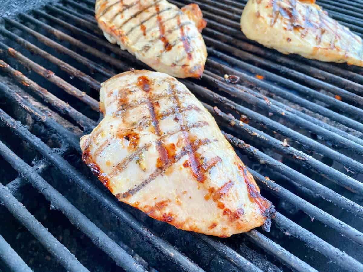 Three chicken breast with grill marks on top of black grill grates.