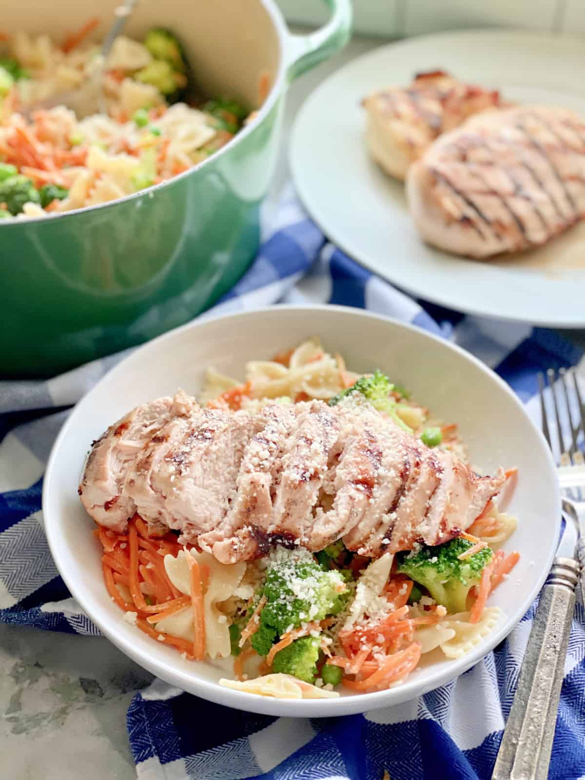 Bowl full of Grilled Chicken Pasta with veggies with a plate of chicken breast in background.