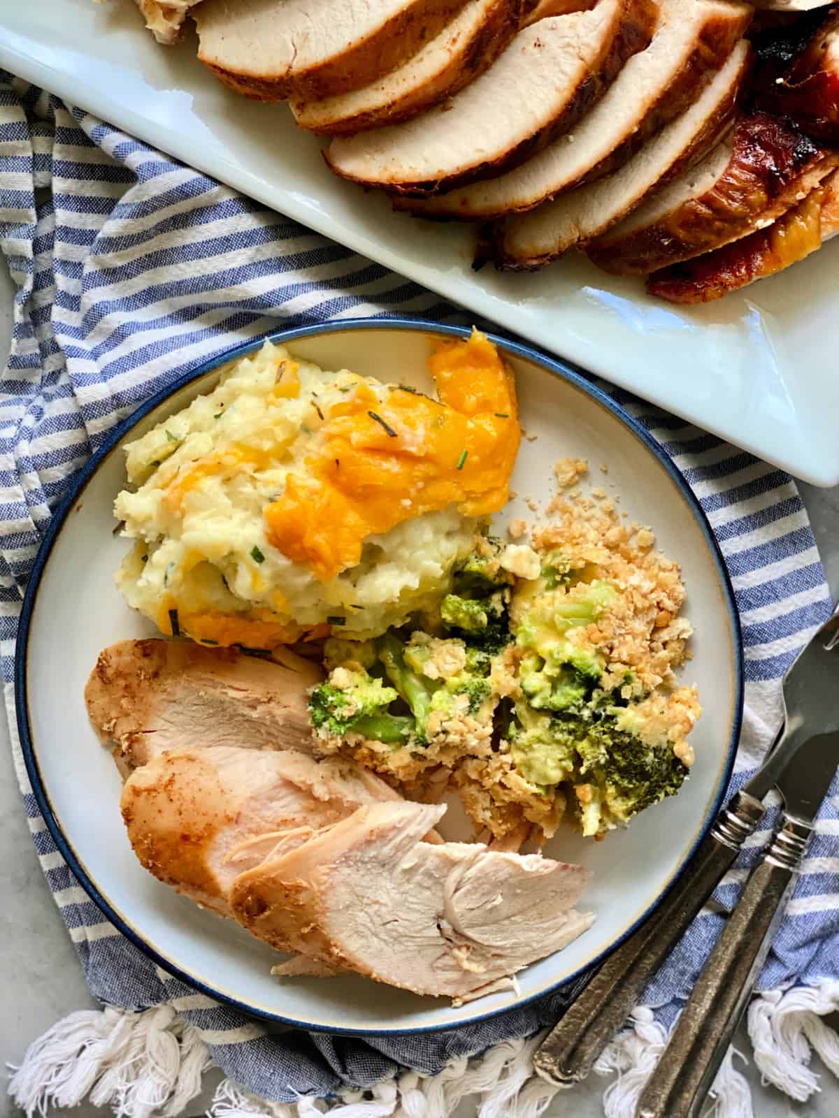 Top view of a plate filled with three slices of turkey bresat, mashed potatoes, and casserole with a platter of sliced turkey on the side.