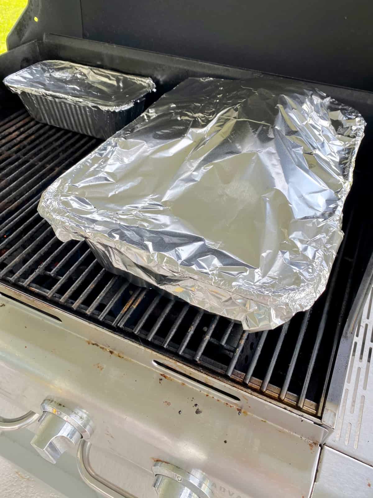 Two metal pans wrapped with aluminum foil on top of a grill.