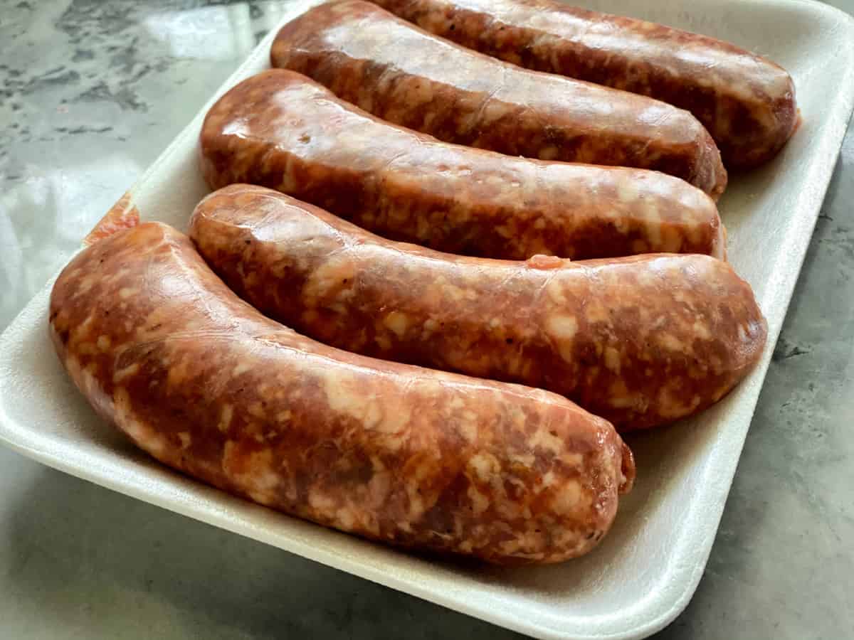 Five raw sausages on a white styrofoam tray sitting on a marble countertop.