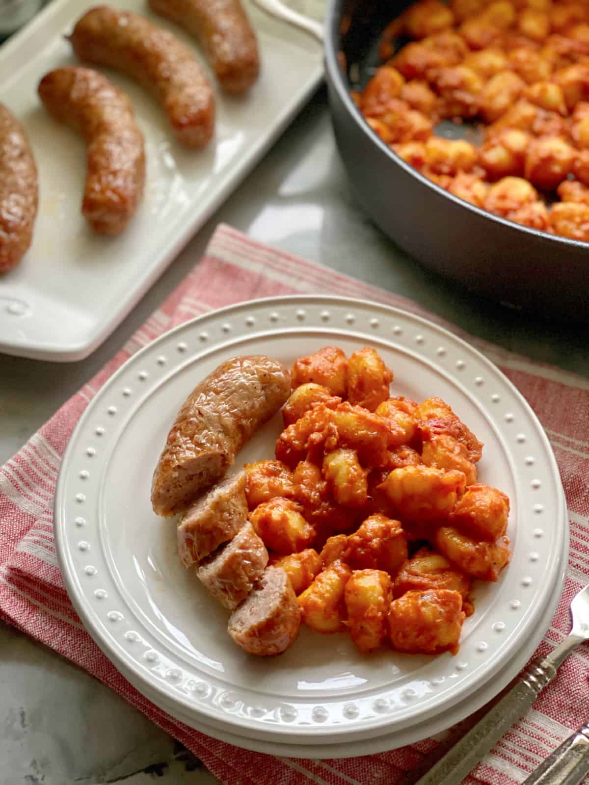 White plate filled with a sliced sausage link with tomato sausage with gnocchi.