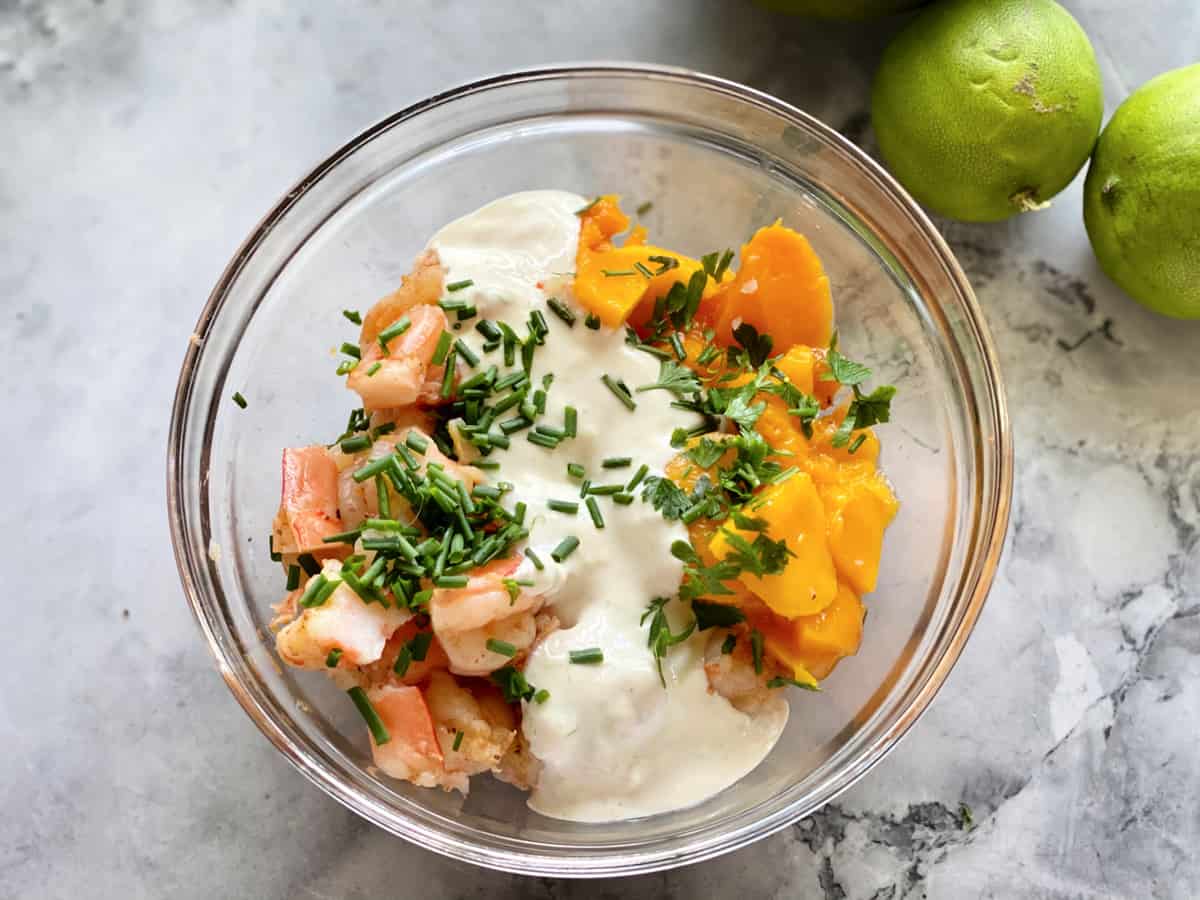 Top view of a glass bowl on a marble counterotp with mago, sour cream, chives, and shrimp.