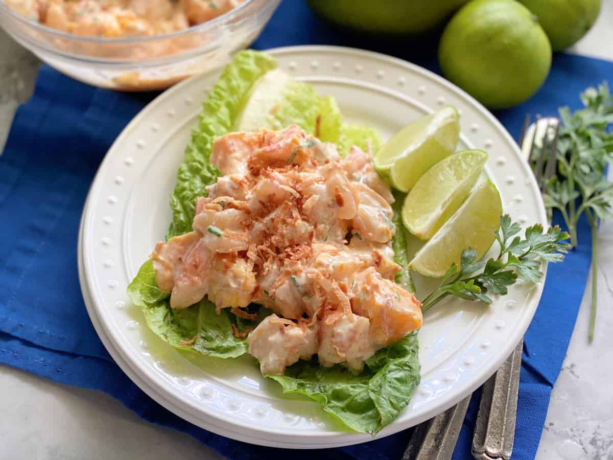 White plate with lettuce leaves and shrimp with sauce.