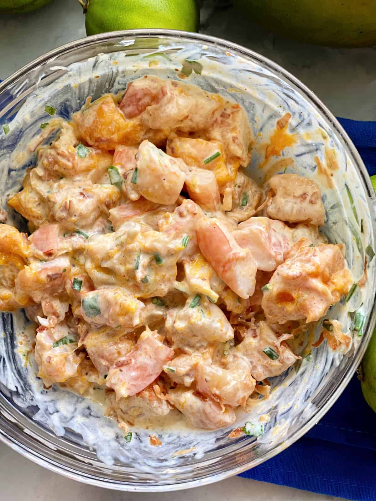 Top view of a glass bowl of shrimp with sauce and mango.