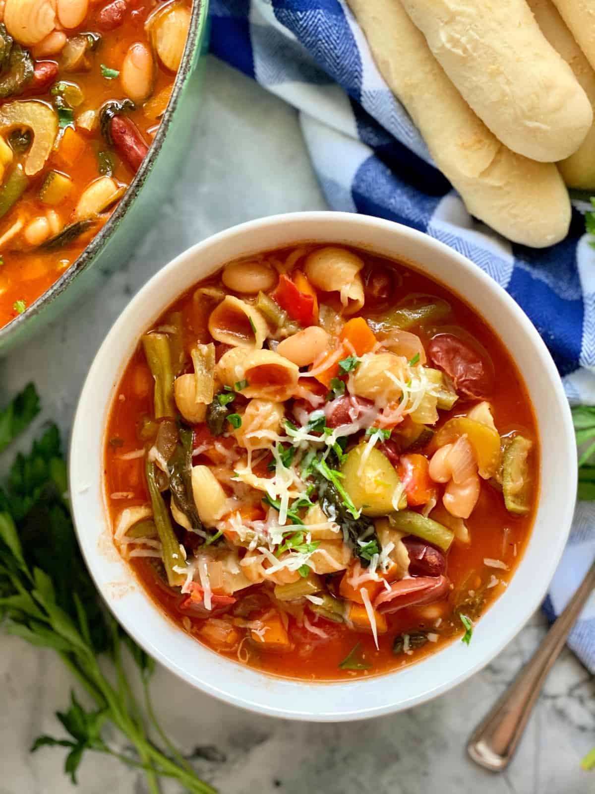 Top view of a white bowl filled with minestrone soup with breadsticks.