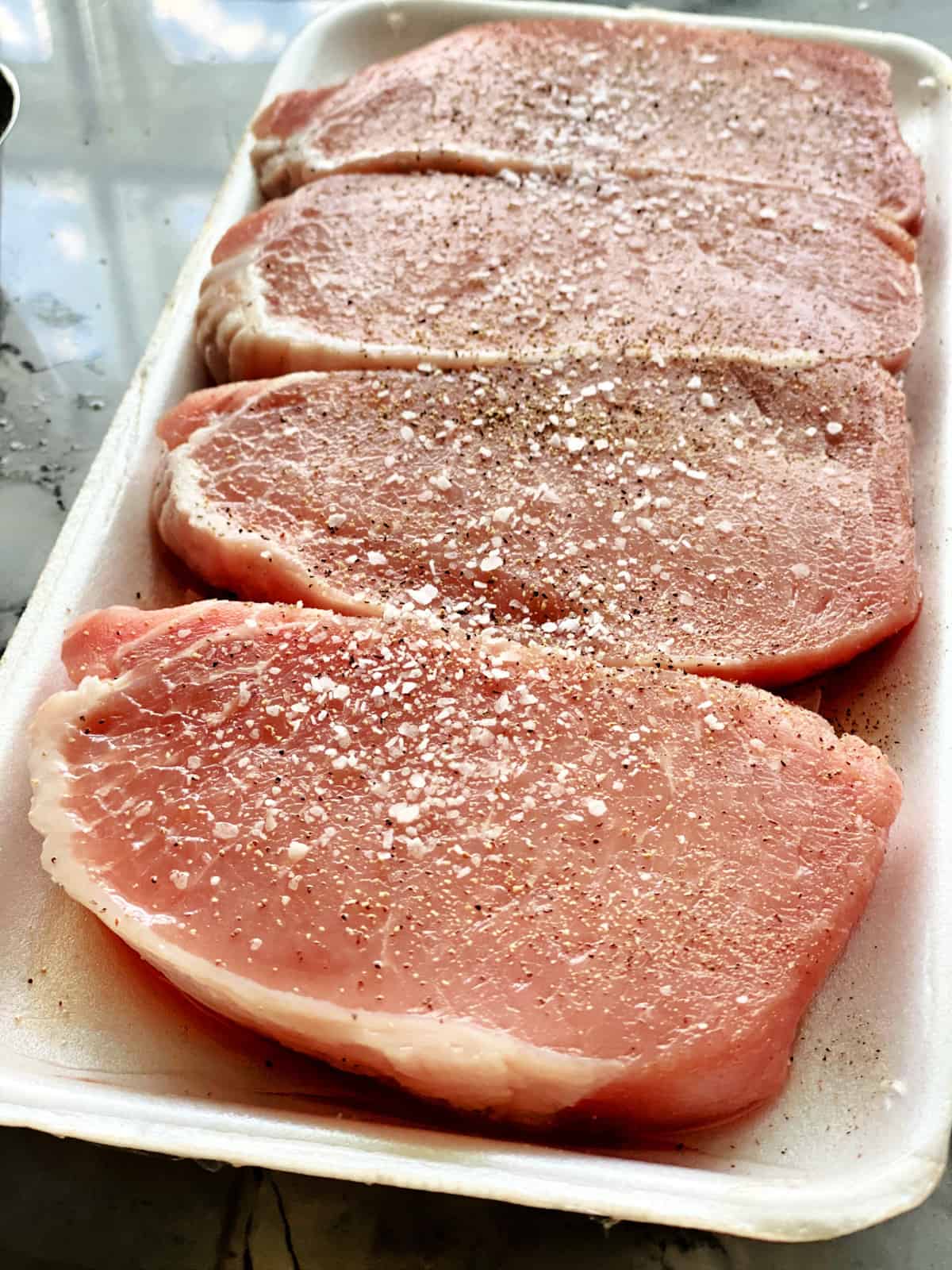 Four boneless porkchops seasoned on a white styrofoam tray.