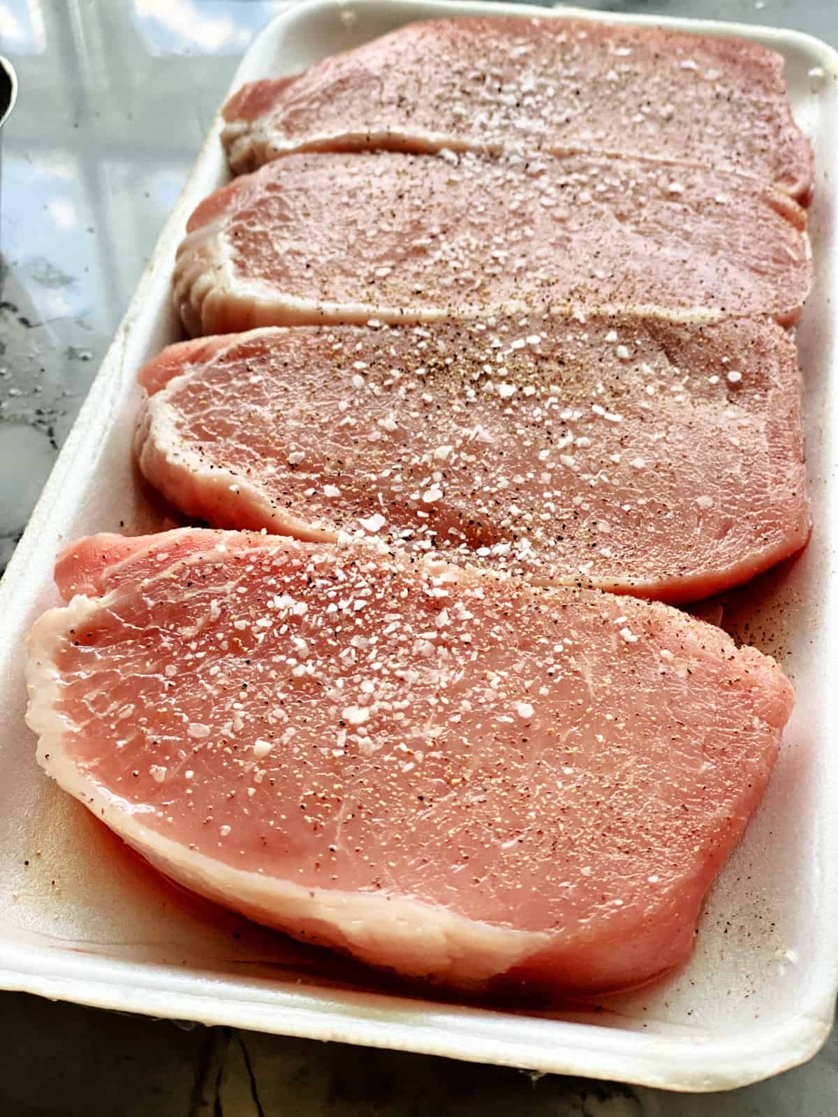 Four boneless porkchops seasoned on a white styrofoam tray. 