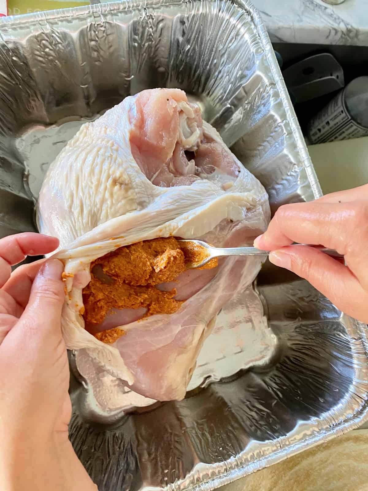 Top view of a female hand holding open the skin of a turkey breast with butter/rub mixture.