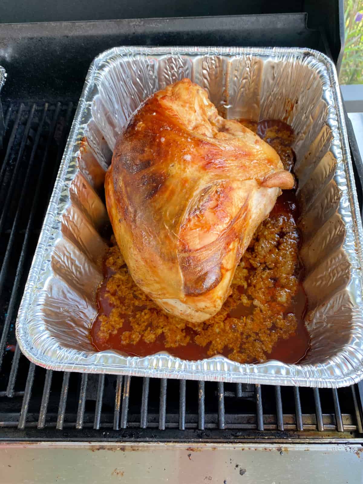Browned turkey breast in a metal pan with juices over a grill grate.