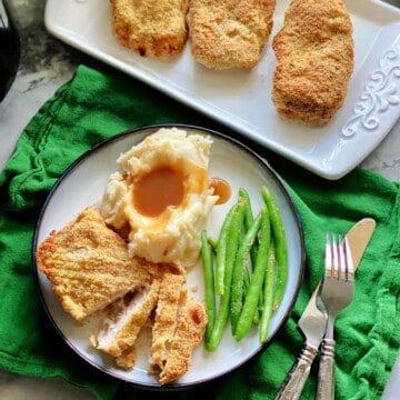 Sliced pork chops, mashed potatoes, and green beans on a plate.