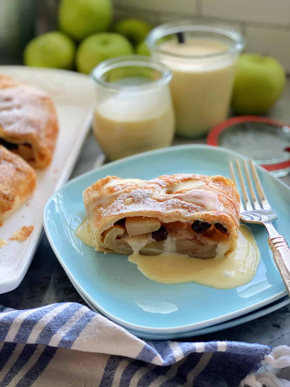 Two square light blue plates with a slice of Apple Strudel with vanila sauce.