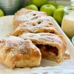 White platter with a puff pastry Apple Strudel sliced with apples in background.