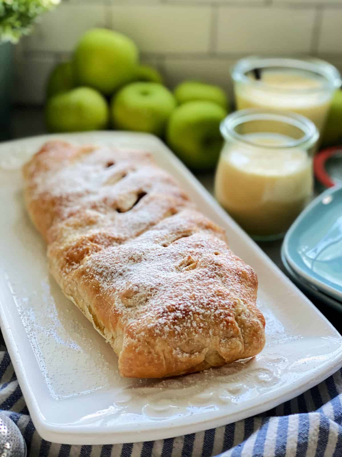 White platter with Apple Strudel with vanilla sauce jars in background.