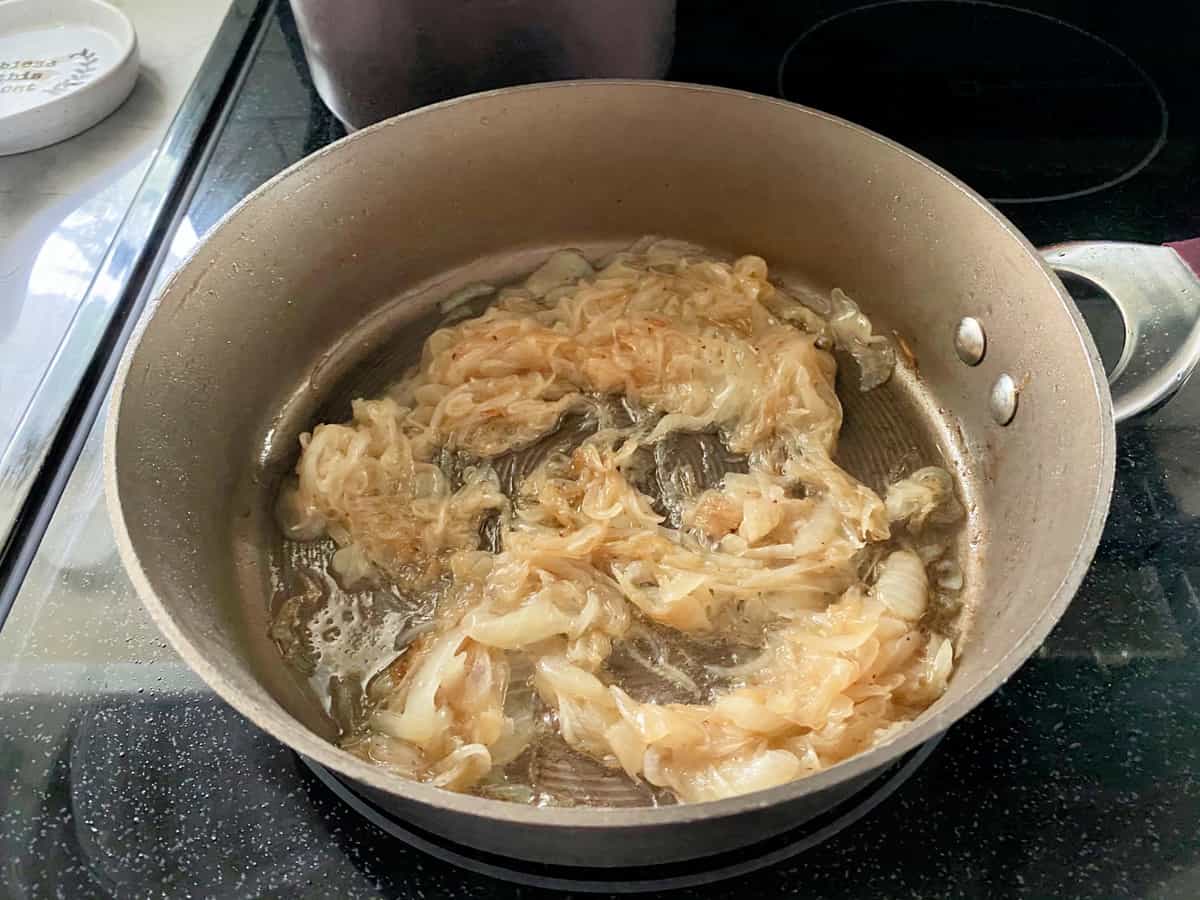 Carmelized onions in a brown skillet on a glass top cooking top.