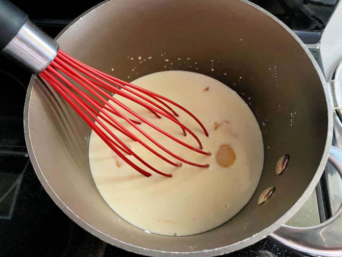 Brown pot with a red silcone balloon whisk in milk and egg.