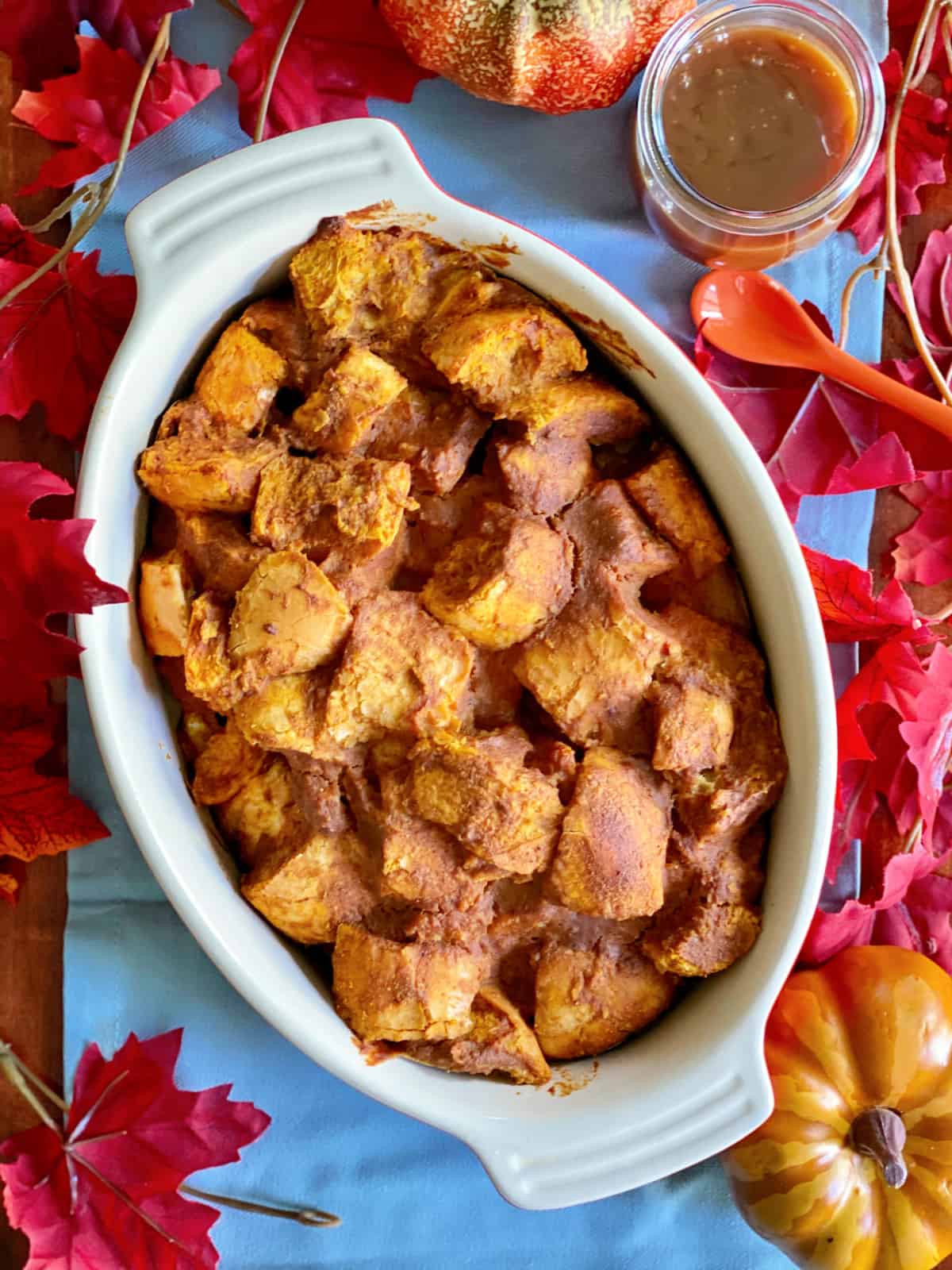 Top view of pumpkin bread pudding in an oval dish with fall leaves around it.