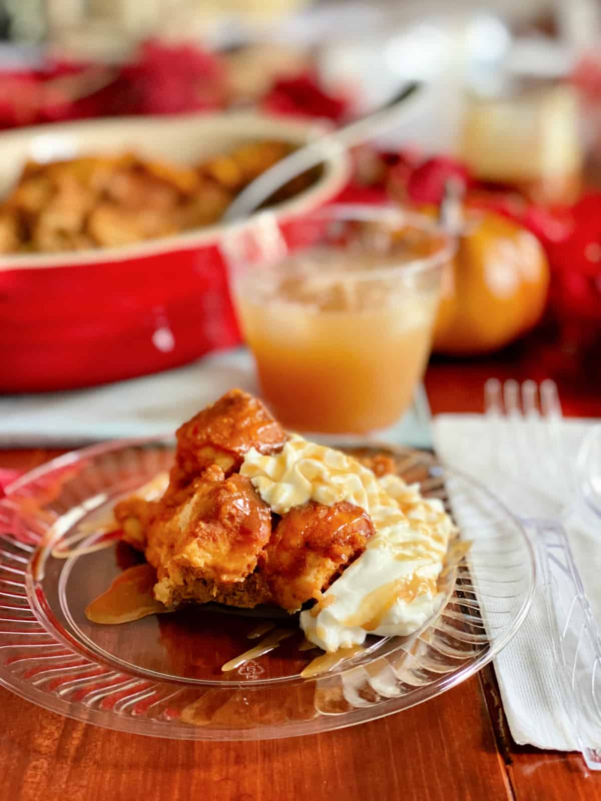 Clear plastic Chinete plate with bread pudding and whipped cream on it, with a paper napkin and plastic fork next to it.