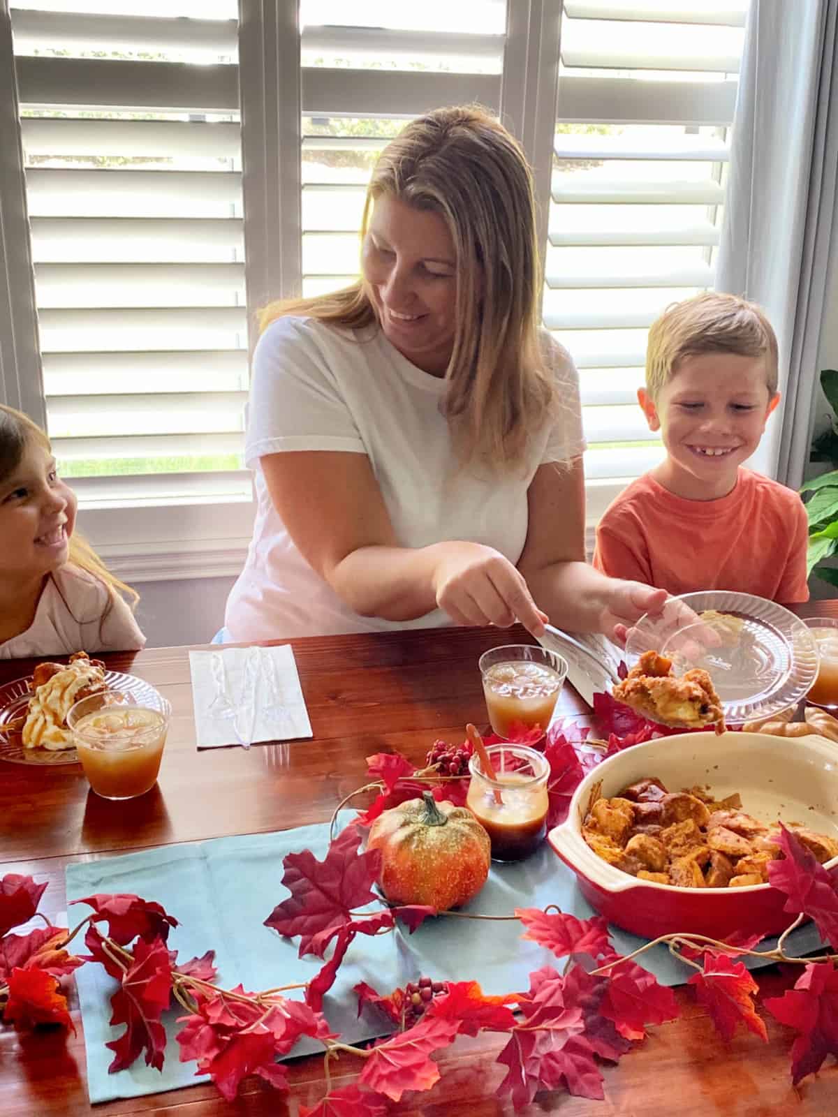 Mom dishing bread pudding on plastic Chinet plate with kids looking at her and smiling.