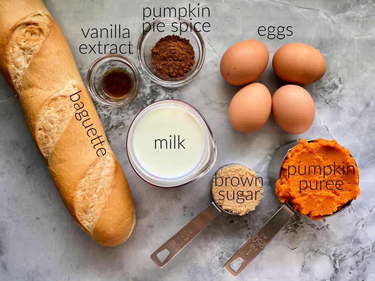 Ingredients on counter: baguette, milk, vanilla extract, pumpkin pie spice, eggs, brown sugar, and pumpkin puree.