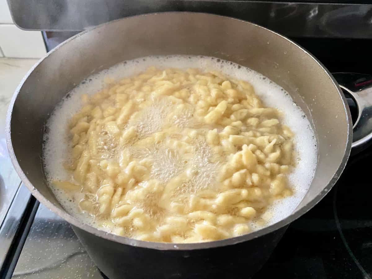 Black pot with boiling spaetzle in water on a glass stove top.