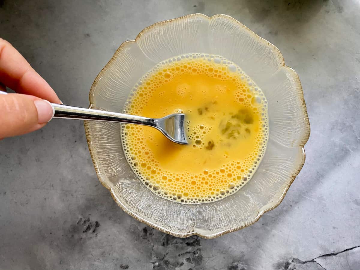 Small glass bowl with a female hand whisking an egg with a fork.