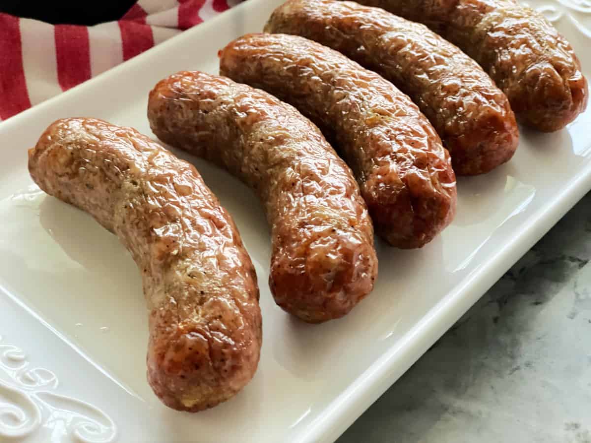 Five cooked brat links on a white tray.