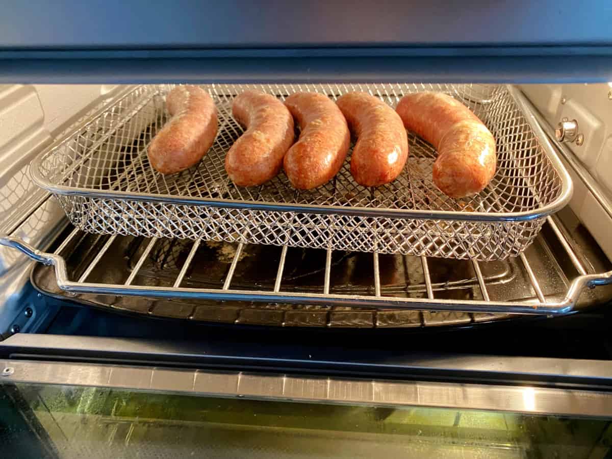 Five brat links in an air fryer oven cooking.