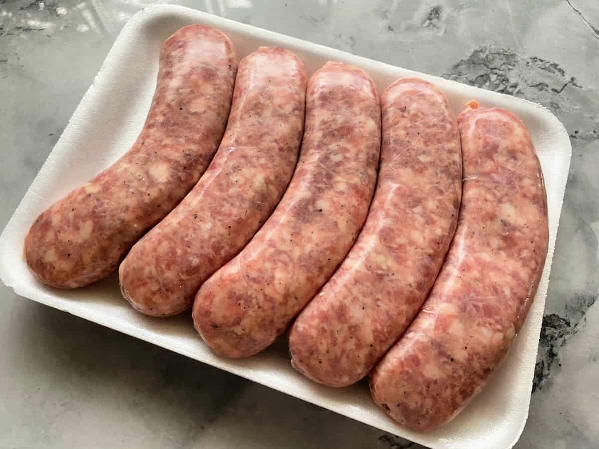 White styrofoam tray with 5 raw brats on a marble countertop.