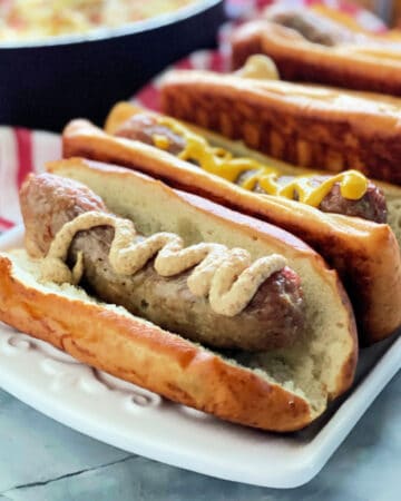 White platter filled with 4 sausages in buns.