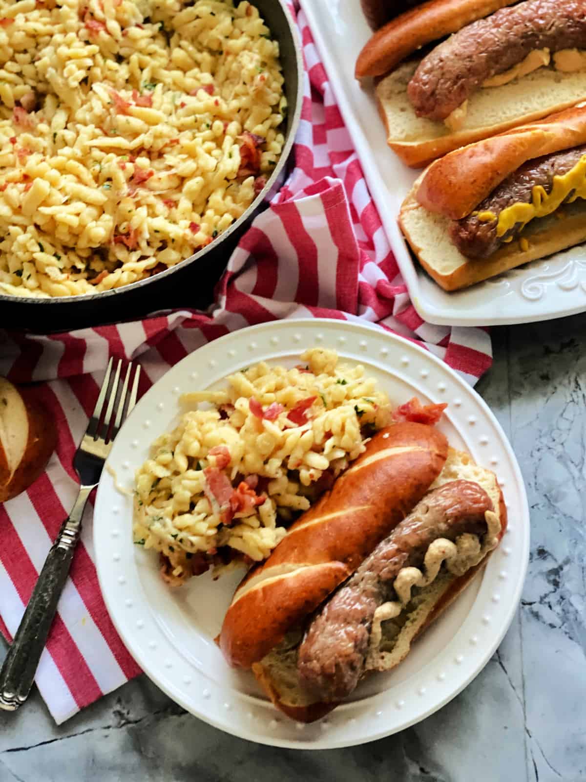 Top view of a white plate filled with a pretzel bun with a brat, mustard, and spaetzel.