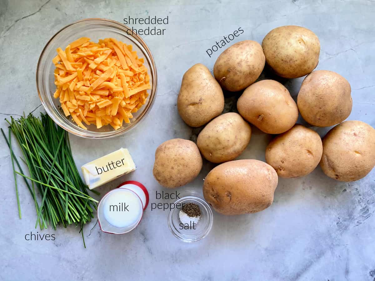 Ingredients on counter: potatoes, cheddar cheese, chives, butter, milk, black pepper, and salt.