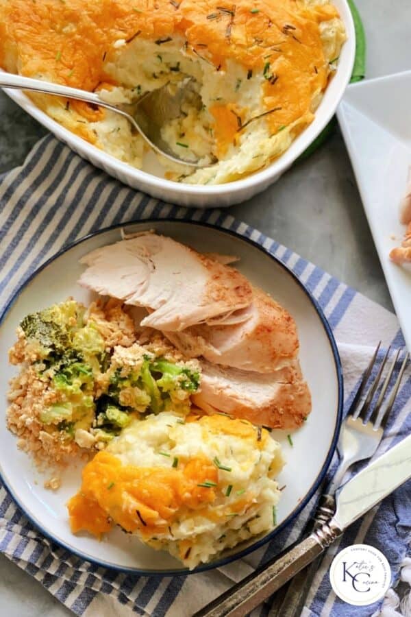 Top view of a plate full of turkey, broccoli casserole and mashed potatoes with a casserole dish full of potatoes on the side and logo onthe right bottom corner.