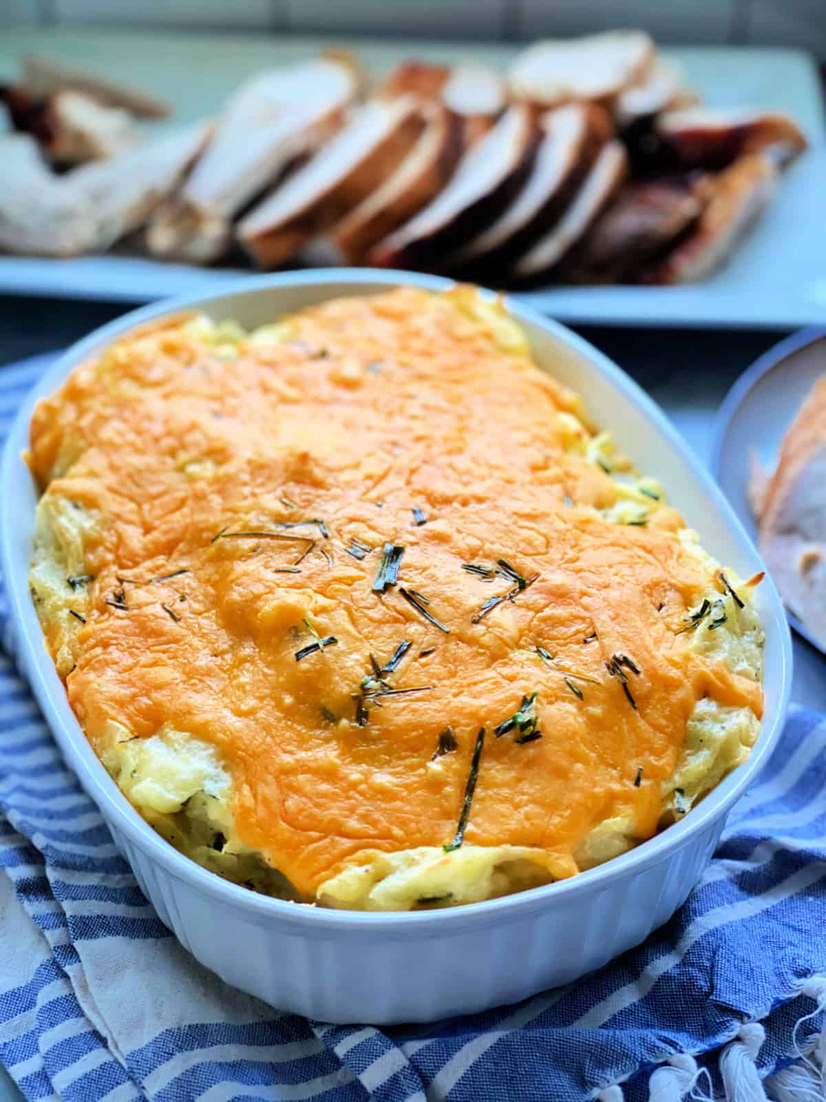 White baking dish filled with mashed potatoes and cheese topped with chives.