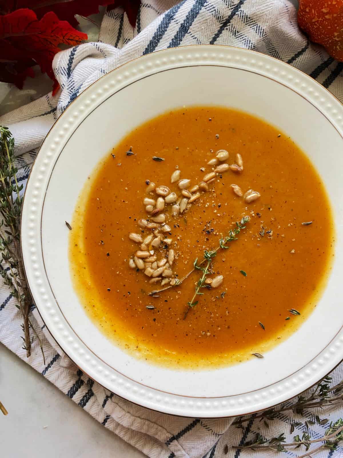 Top view of a close up of a white bowl filled with orange squash soup with nuts.