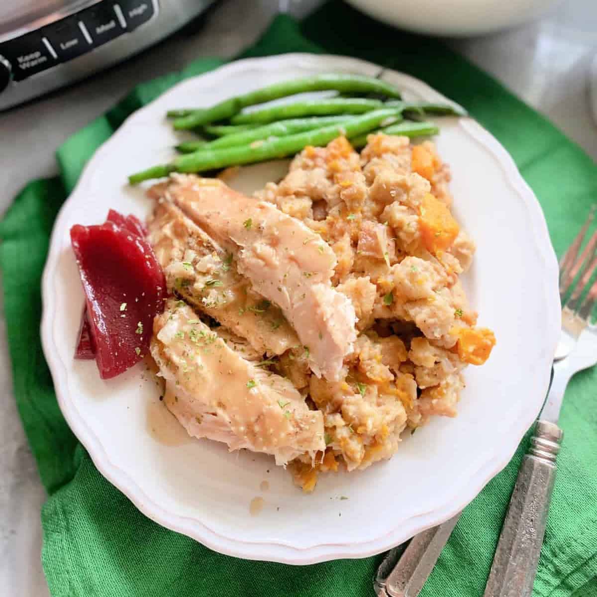 White plate filled with turkey, stuffing, cranberry and green beans.