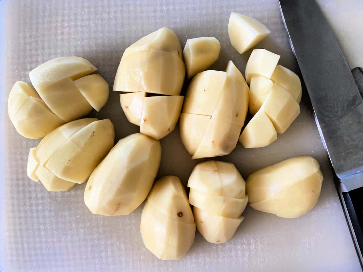 White potatoes peeled and quartered on a white cutting board with a sanduko knife next to it.